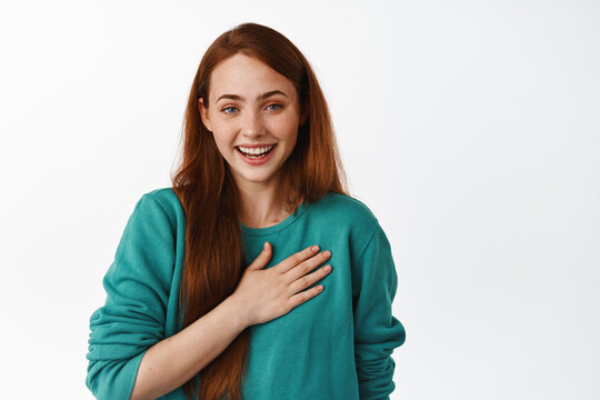 Happy beautiful woman with red hair, laughing and hold hand on heart, appreciate compliment, look thankful, smiling flattered and pleased white background