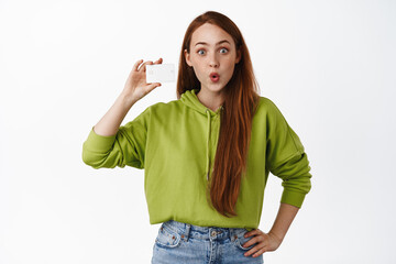 Portrait of surprised and excited redhead girl shows small, little size, tiny thing, looks...