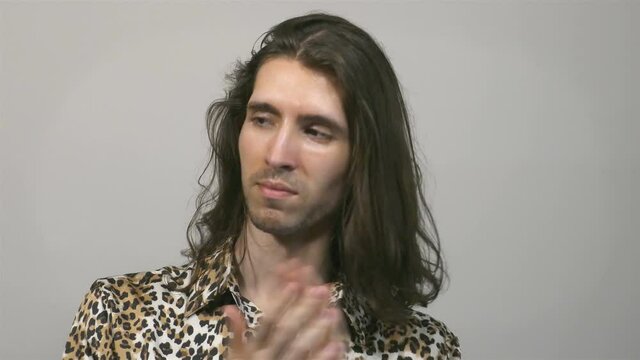 Young long-haired man clapping and looking around, wearing leopard pattern shirt