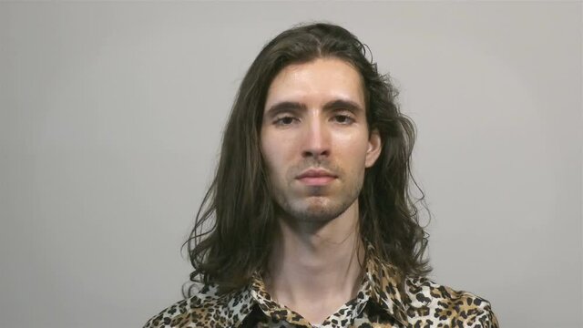 Young long-haired man waving hand to camera, wearing leopard pattern shirt