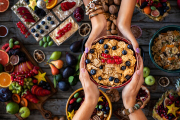 Hands of two women sharing their breakfast bowl. Breakfast with fresh fruit and muesli. 