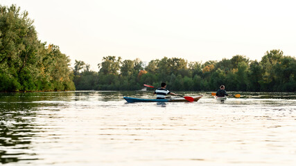 Fototapeta na wymiar Two young guys paddling kayak on a lake surrounded by beautiful nature