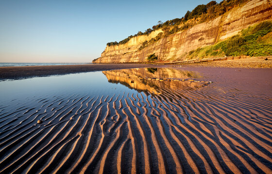 Shanklin beach on the isle of wight, with ripples in the sand and reflection of cliffs in the pool of water.
