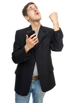 Young handsome tall slim white man with brown hair with mobile phone doing winning gesture in black blazer isolated on white background