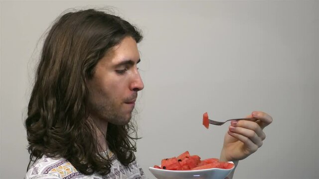 Young long-haired man eating freshly cut watermelon using fork