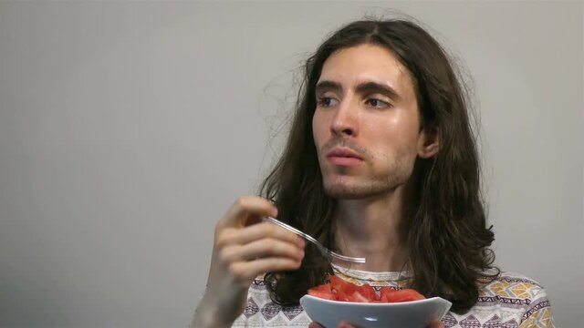 Young long-haired man eating freshly cut watermelon using fork