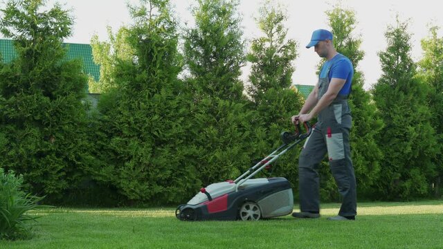 Young gardener in overalls uses a lawn mower on the plot