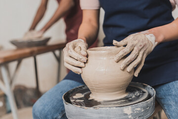partial view of young african american woman shaping wet clay pot on wheel with sponge in pottery