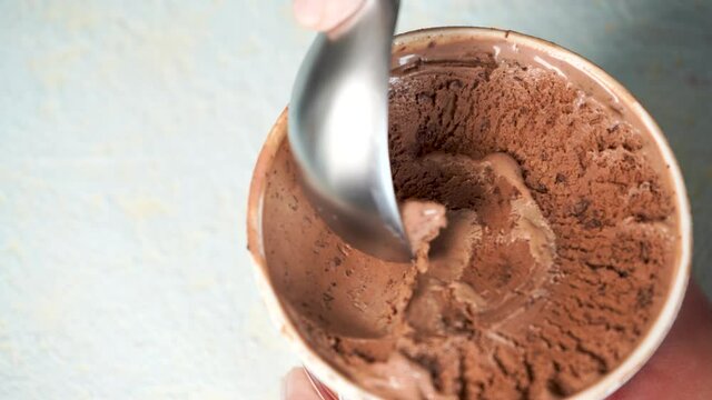 Female hand making a chocolate bites ice cream ball with metal spoon 4K close up