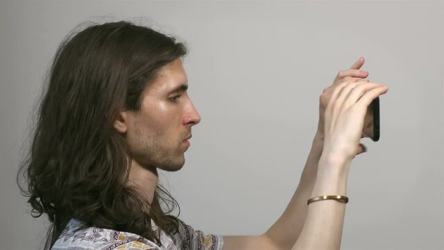 Young long-haired man working with smartphone, side view,