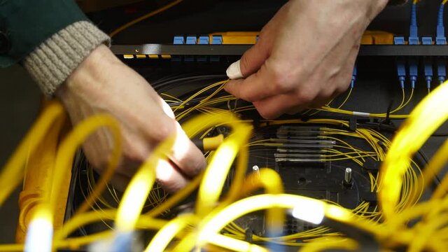 Worker connects optical line internet wire in connection box. Service man soldering optical fiber. Internet service provider engineer working in server room with the optic fiber and router wiring.