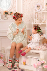 Fototapeta na wymiar Adorable little girl with her mother in curlers paint their fingernails. Copies mom's behavior. Mom teaches her daughter to take care of herself. Beauty day