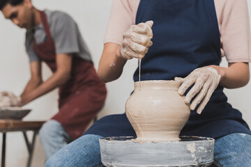 partial view of young african american woman squeezing sponge while shaping wet clay pot on wheel near blurred man in pottery