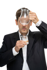 Young handsome tall slim white man with brown hair looking through glass pitcher of water in black blazer isolated on white background