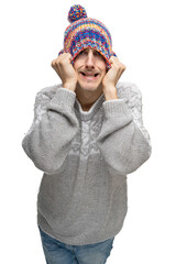 Young handsome tall slim white man with brown hair pulling his colorful winter hat in gray jumper isolated on white background