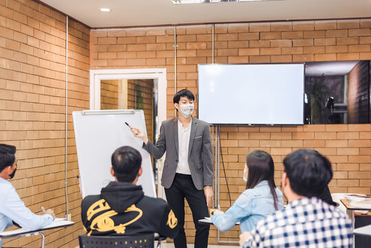 business cooperation : Young asian male coach or speaker make flip chart presentation to diverse businesspeople at meeting in office. Male tutor or trainer present project to diverse colleagues.