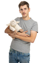 Young handsome tall slim white man with brown hair in gray shirt in blue jeans with plush sheep isolated on white background
