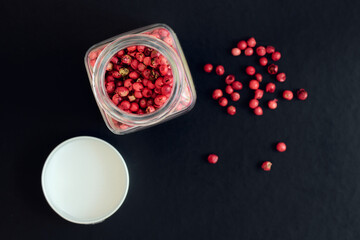 Pink peppercorns in a glass jar on a dark background, shallow depth of sharpness, view above