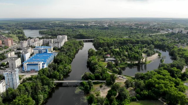 Panoramic drone view of a green city in northern Europe. Drone shot on an island with sandy beaches. Pedestrian bridge over the Psel river in Ukraine, the city of Sumy.People are relaxing on the beach
