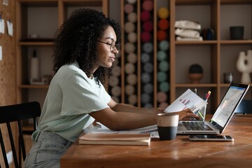 Young beautiful african american woman using her laptop while sitting in chair at her working place