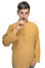 Young handsome tall slim white man with brown hair holds incense stick in his hand in ochre shirt isolated on white background