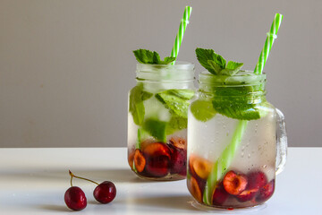 Cold drinks in small bottles. Cherries and mint lemonade. Mojito coctail. Summer iced refreshment drink. Summer cold mint coctails with berries. Mason jar glass with cold drink.