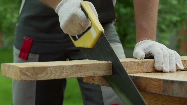 Man carpenter saws a wooden board with a hand saw. 