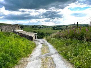 Track with wild plants, leading to a stone built farm, and hills in the far distance, on a cloudy day in, Stainland, Huddersfield, UK