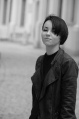 A happy young girl in a black leather jacket and short hair is sitting at a table. Black and white portrait of a smiling woman	