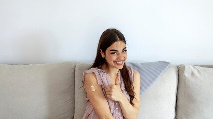 Happy vaccinated woman showing arm with plaster bandage after Covid-19 vaccine injection, posing over white background, smiling to camera. Young woman after vaccination. Virus protection. COVID-2019.