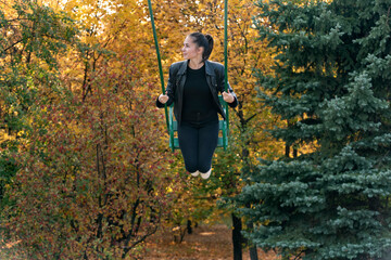 Beautiful young woman swinging on a swing in the autumn park. Joyful moments of life
