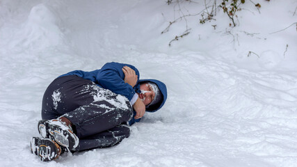 Frozen man in a blue jacket and hat lying down covered snow and frost, trying to stay warm on a...