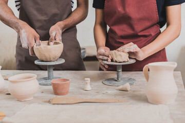partial view of young african american couple in aprons making clay pots on table with equipment in...