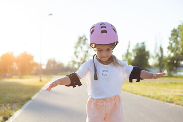 Little caucasian girl on in-line skates with full protective equipment. Child rollerblading in the...