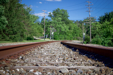 Fototapeta na wymiar Close up of train tracks railroad crossing ahead with green trees and bright blue sky 