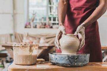 partial view of young african american man sculpting pot on wheel near plastic box with water in pottery