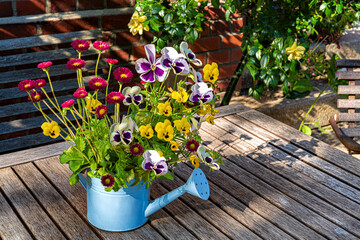 Watering can with beautiful wildflowers on the wooden table in garden.Sunny summer day in countryside.