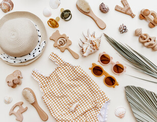 Flat lay Summer kids accessories on brown background. Cute retro swimsuit, straw hat, sunglasses, bib, wooden toys and seashells, summer holiday concept