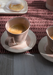 Closeup view of an elegant white pink ceramic cup of coffee over a pinkish tablecloth.
