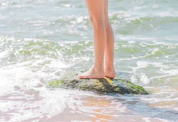 legs of a young girl stand on a stone in the water near the seashore. summer vacation concept