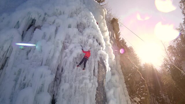 Wide shot of a male athlete doing a vertical ice climb, kicking front crampons into the ice and swinging an ice tool