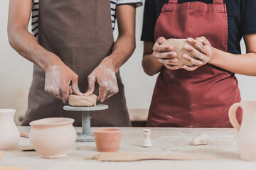 partial view of young african american couple in aprons making clay pots on table with equipment in...