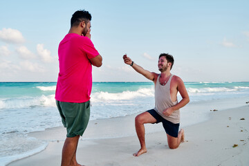 homosexual couple of two men, making a marriage proposal on the coast of cancun beach in the mayan rivera maya mexico, with a turquoise sea in the background.