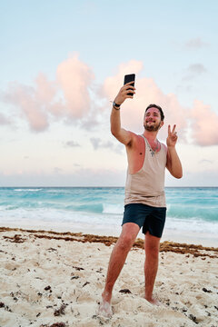 caucasian man with a cell phone in his hands taking a selfie picture at sunset at the sea of cancun, vertical orientation