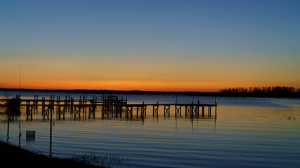 Fototapeta na wymiar Fishing Pier Sunrise/Sunset Over Still Water mirroring a Vibrant Colored Sky.