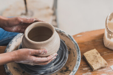 partial view of young african american woman modeling wet clay pot on wheel with hands on bench with sponge in pottery