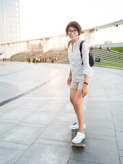 Obraz premium Woman rides skateboard on town square at summer sunset. Summer vibes. Learning new things in adulthood. Millennial learns to skate. Healthy lifestyle.
