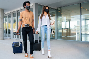 Tourist couple carrying suitcase while walking outdoors.