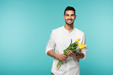 Positive arabian man holding tulip flowers isolated on blue