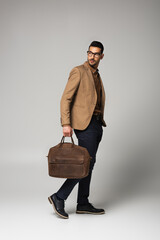 Good looking arabian manager holding handbag while walking on grey background